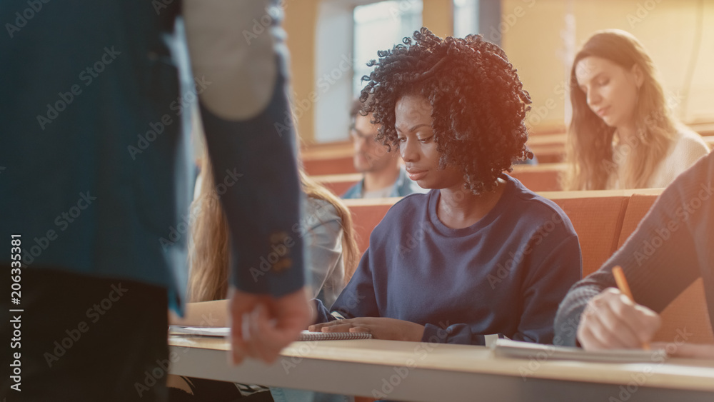 美丽的黑人女学生坐在教室里的同学中间，她在写作