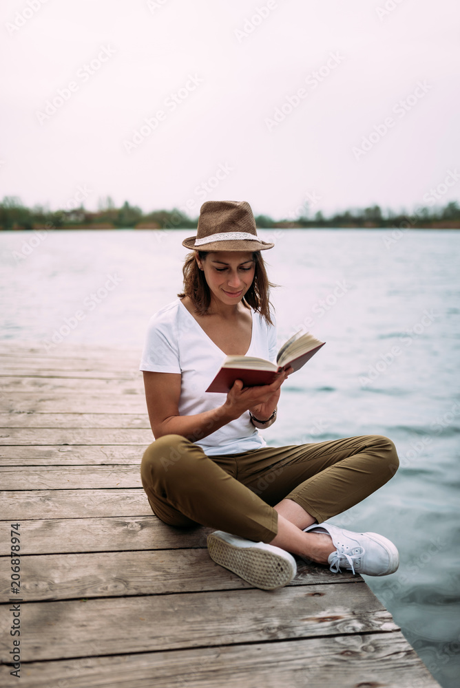 漂亮的年轻女子，戴着帽子，站在木制码头的水边。