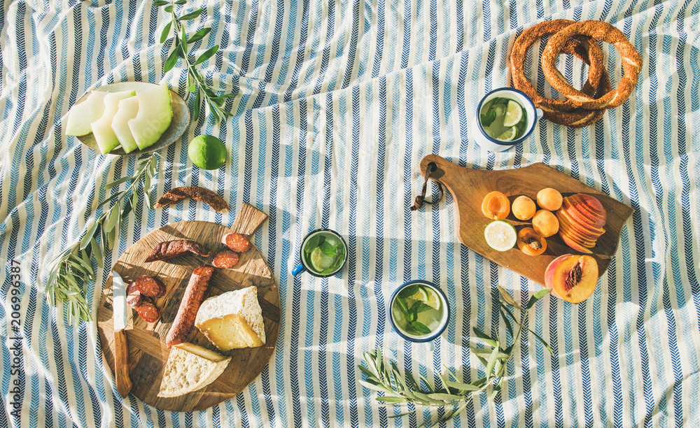 夏季野餐套餐，在条纹毯子上放上水果、奶酪、香肠、百吉饼和柠檬水。