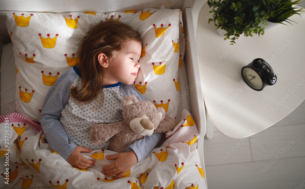 一个小女孩早上抱着玩具泰迪熊睡在床上。