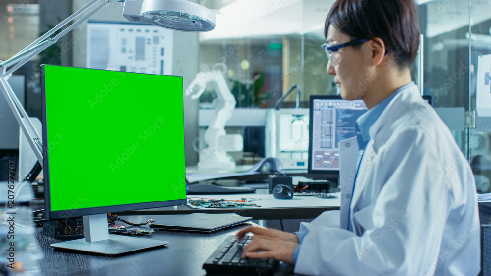 亚洲科学家坐在桌子旁，在一台带绿色屏幕的个人电脑上工作。在B区