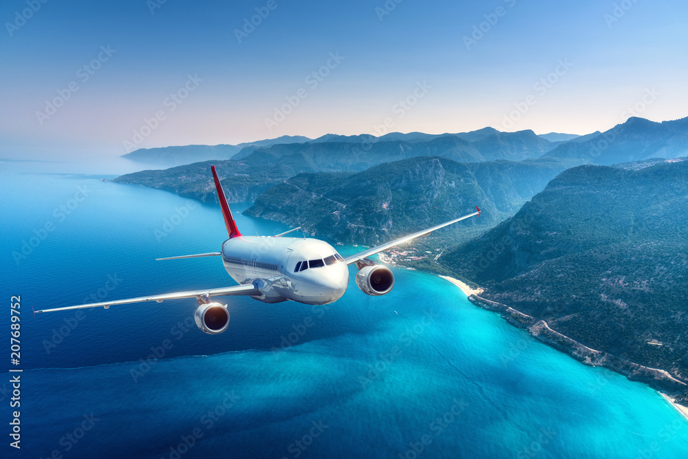 飞机在夏天日出时飞越岛屿和海洋。白色客机的风景