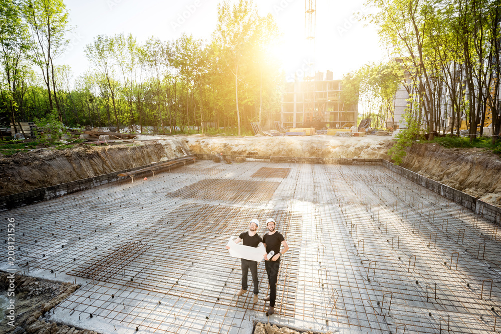 施工现场混凝土基础广角视图，两名建筑工人站在一起