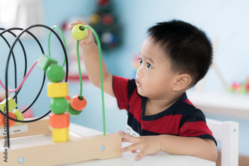Adorable Asian Toddler baby boy sitting on chair and playing with color developmental toys at home..