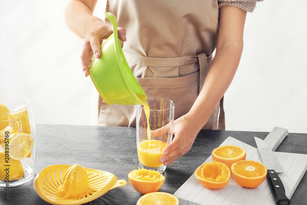 一个女人把美味的柑橘汁倒进桌子上的杯子里