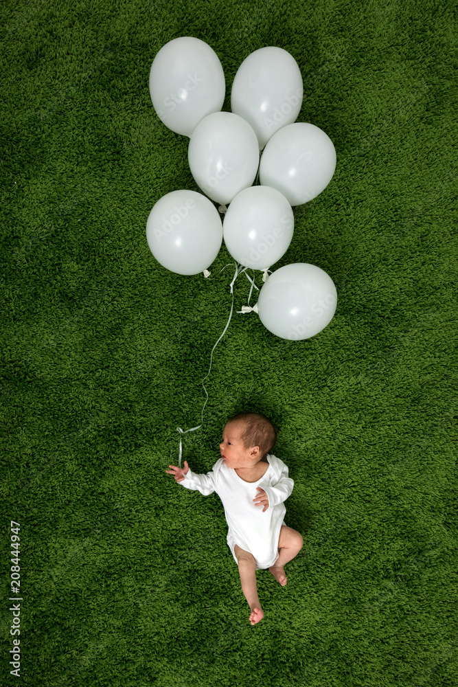 新生儿在绿色地毯上，带着一堆白色气球。人生旅行概念