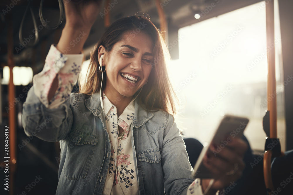 微笑的年轻女子坐在公交车上听音乐