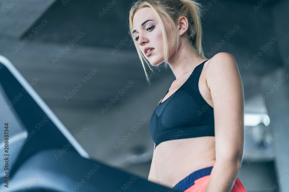 魅力女性在跑步机跑道上锻炼，耳机里的音乐，健身房里的快乐