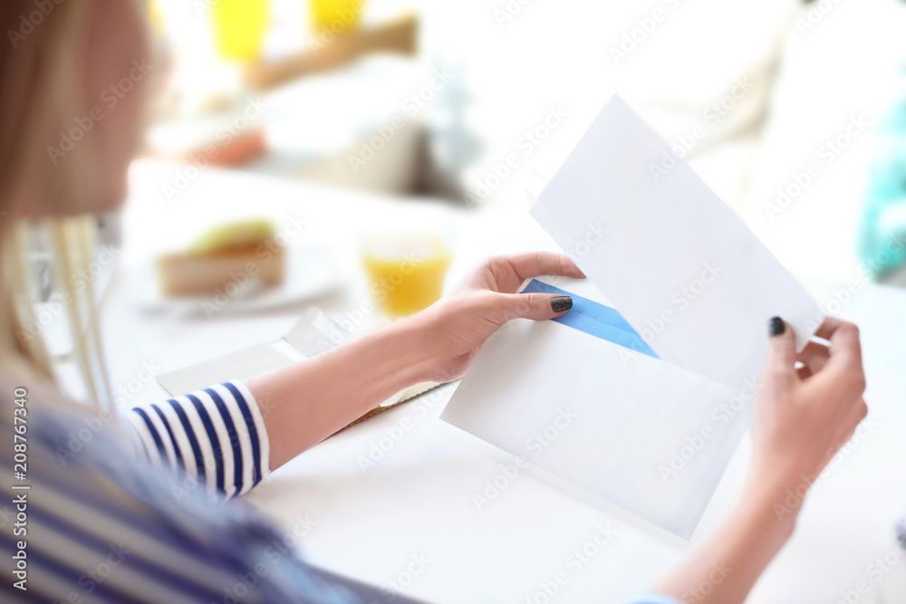 年轻女子在咖啡馆的桌子上把信放进信封。邮件递送