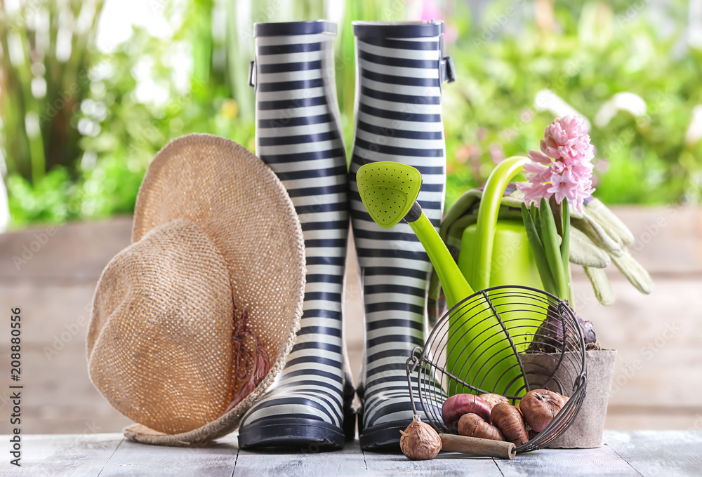 花园木桌上的橡胶靴、球茎和喷壶组成