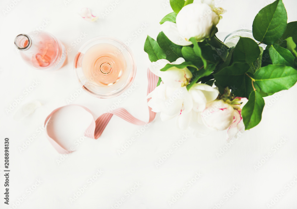 平放在玻璃杯和瓶子里的玫瑰酒，粉红色的装饰丝带和一束牡丹花