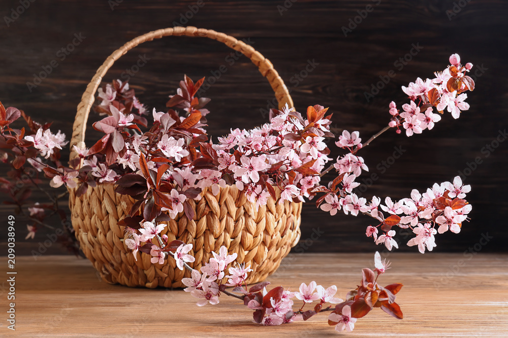 木桌上有美丽的开花树枝的柳条篮