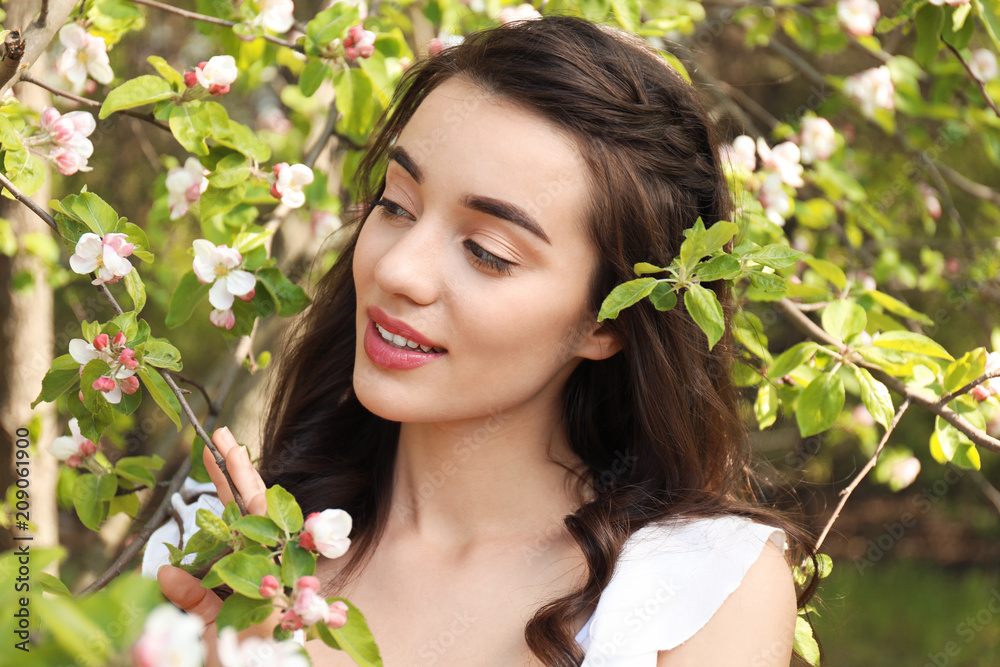 阳光明媚的春天，美丽的年轻女子在开花的树旁