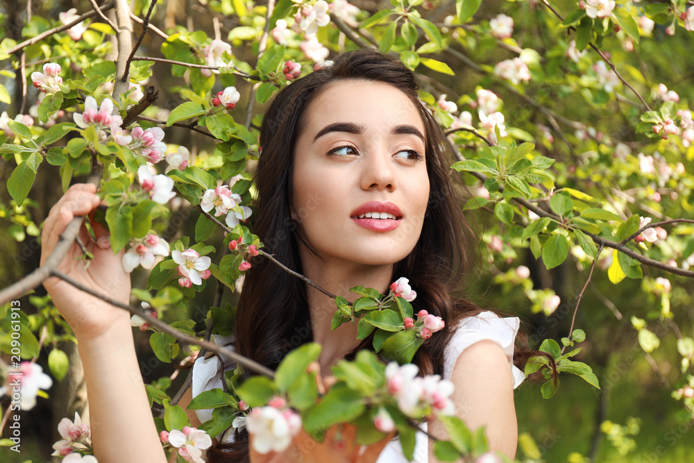 阳光明媚的春天，美丽的年轻女子在开花的树旁