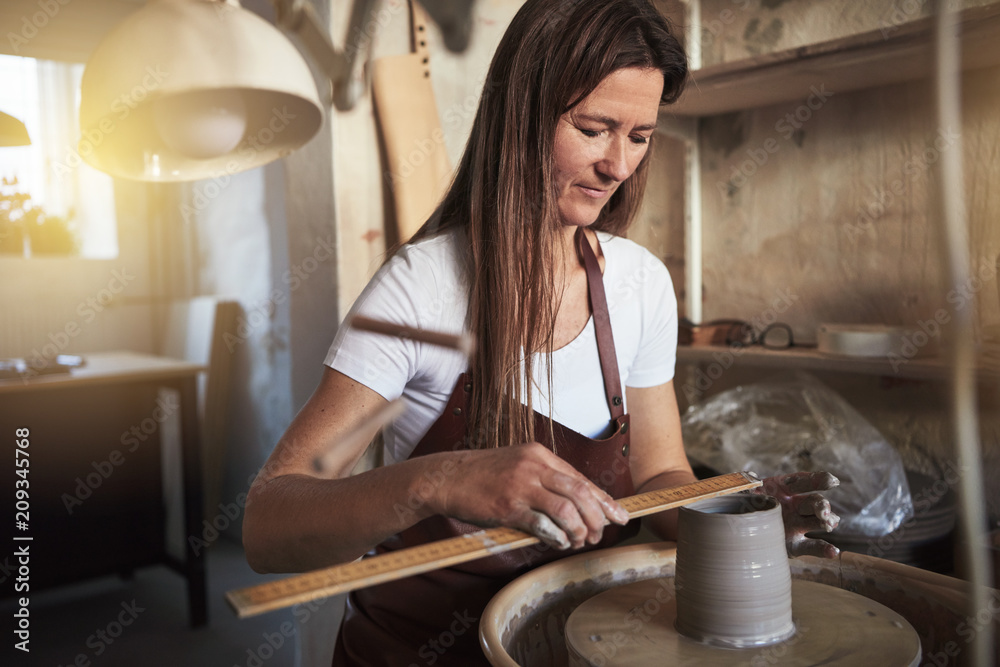 女工匠在她的陶器作坊里测量一个粘土花瓶