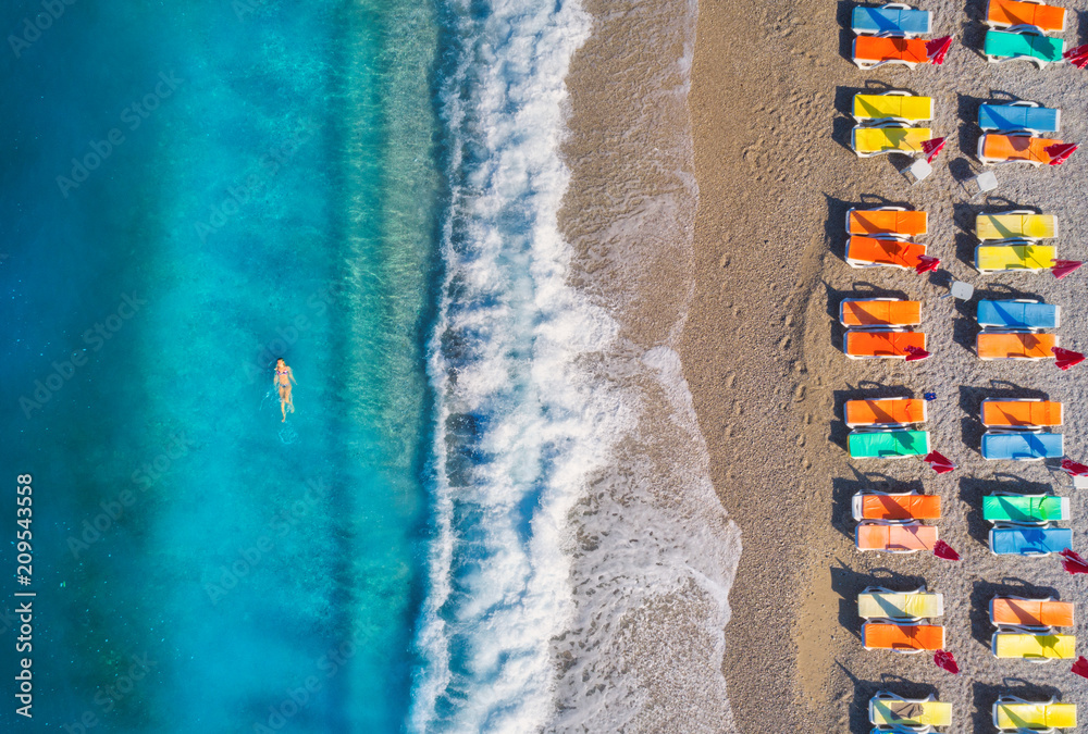 海上和沙滩上游泳女子的鸟瞰图，配有五颜六色的躺椅。年轻女子o