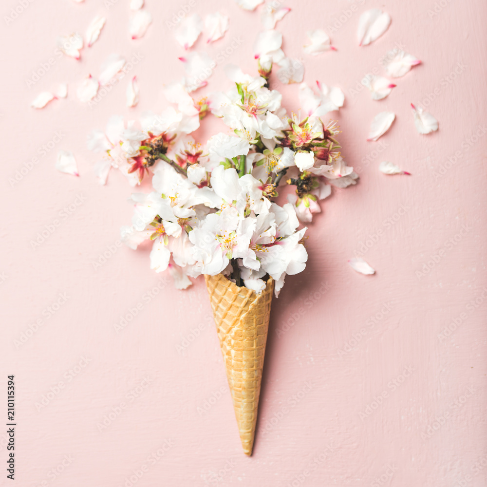 Flat-lay of waffle sweet cone with white almond blossom flowers over pastel light pink background, t