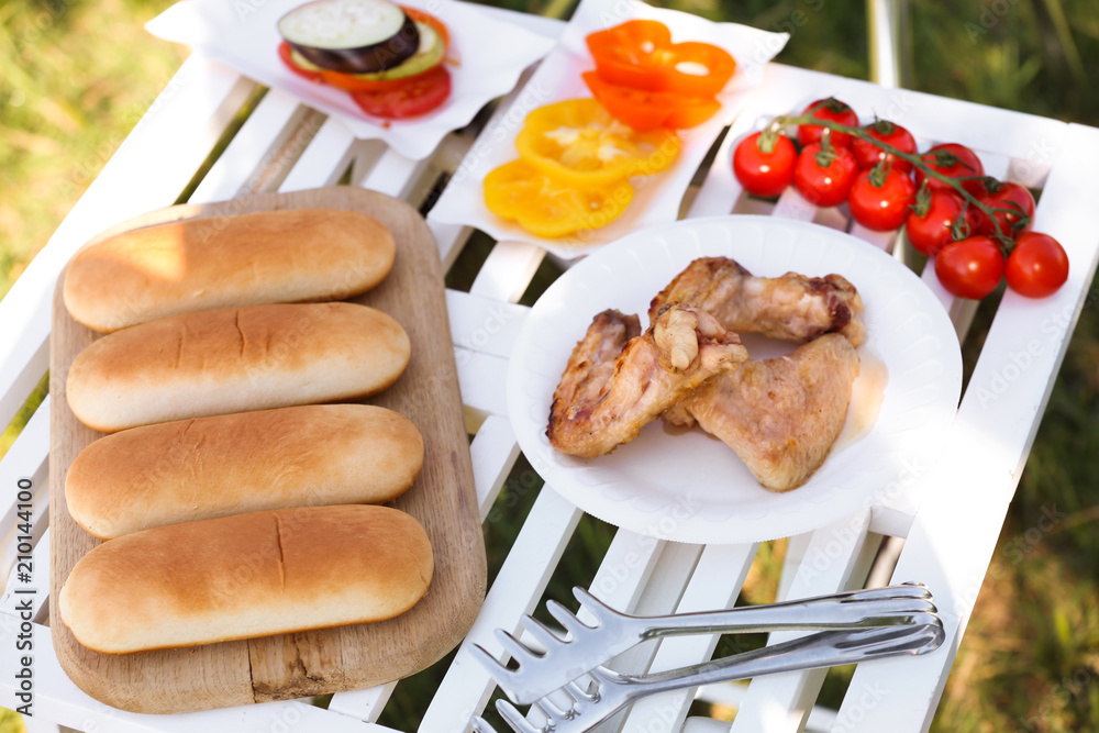 户外餐桌上为夏季野餐准备的烤鸡翅膀、蔬菜和面包的盘子