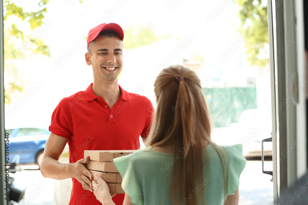 Young man giving pizza boxes to woman at doorway. Food delivery service