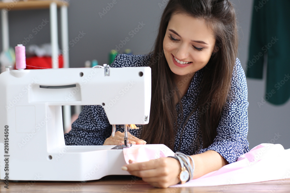 Young female tailor using sewing machine in atelier