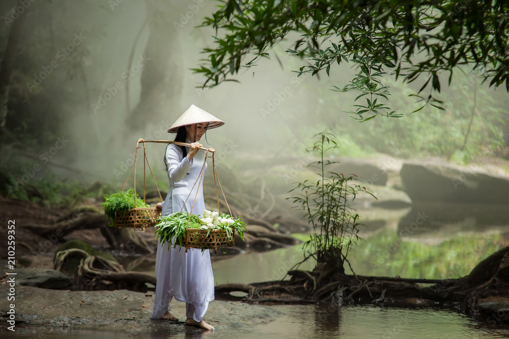 美丽的女人戴着帽子，穿着敖黛传统的越南连衣裙站在森林里。