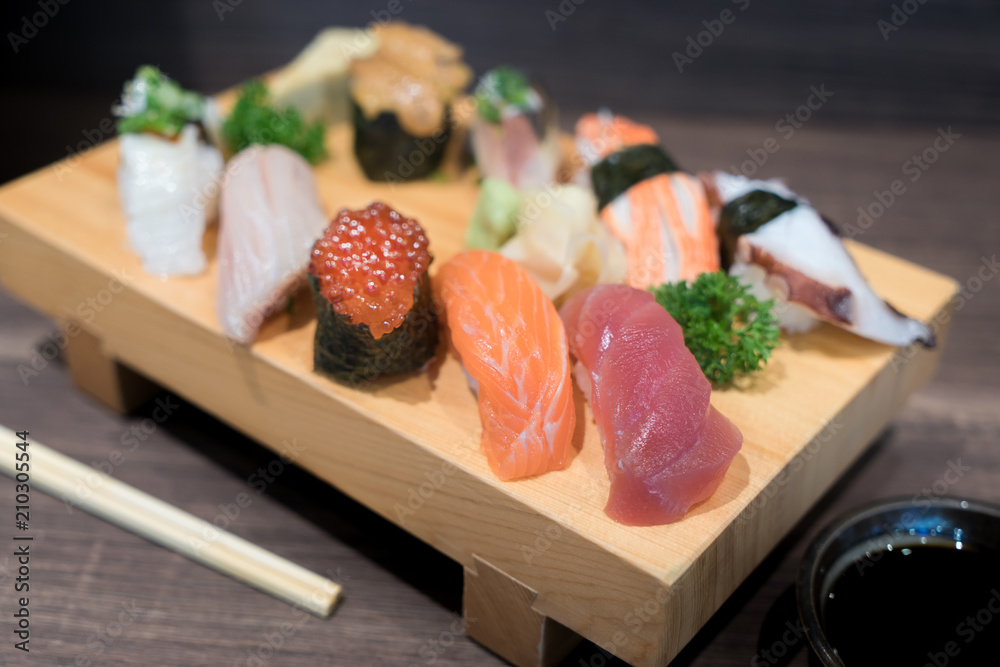 特写寿司和生鱼片混合在黑色木桌上的木盘上。日本食物。