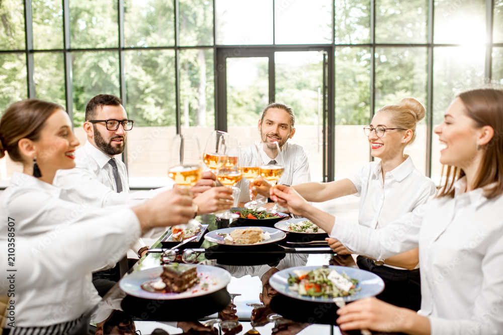 Group of business people dressed in white shirts clinking with wine glasses during a business lunch 