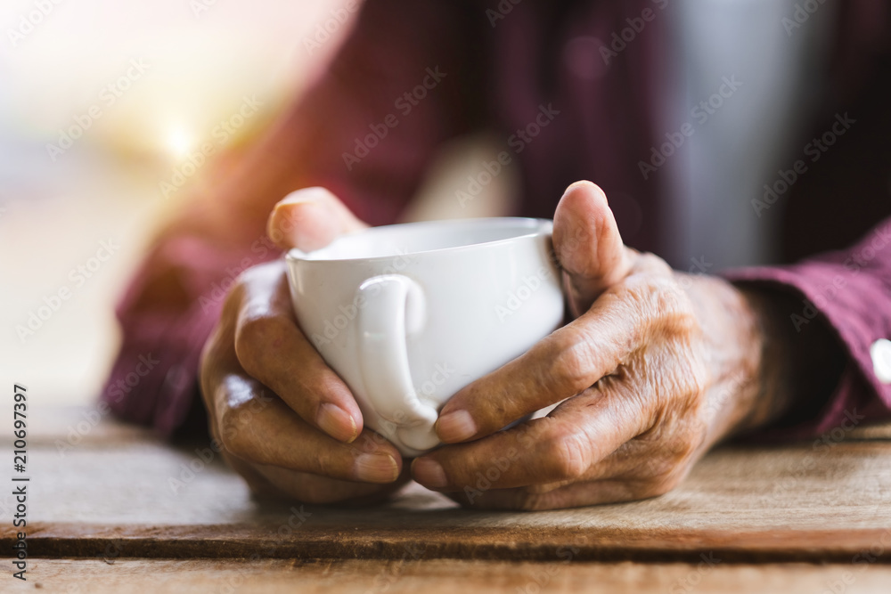 Hands of old man holding cup of coffee on the wood table.vintage tone