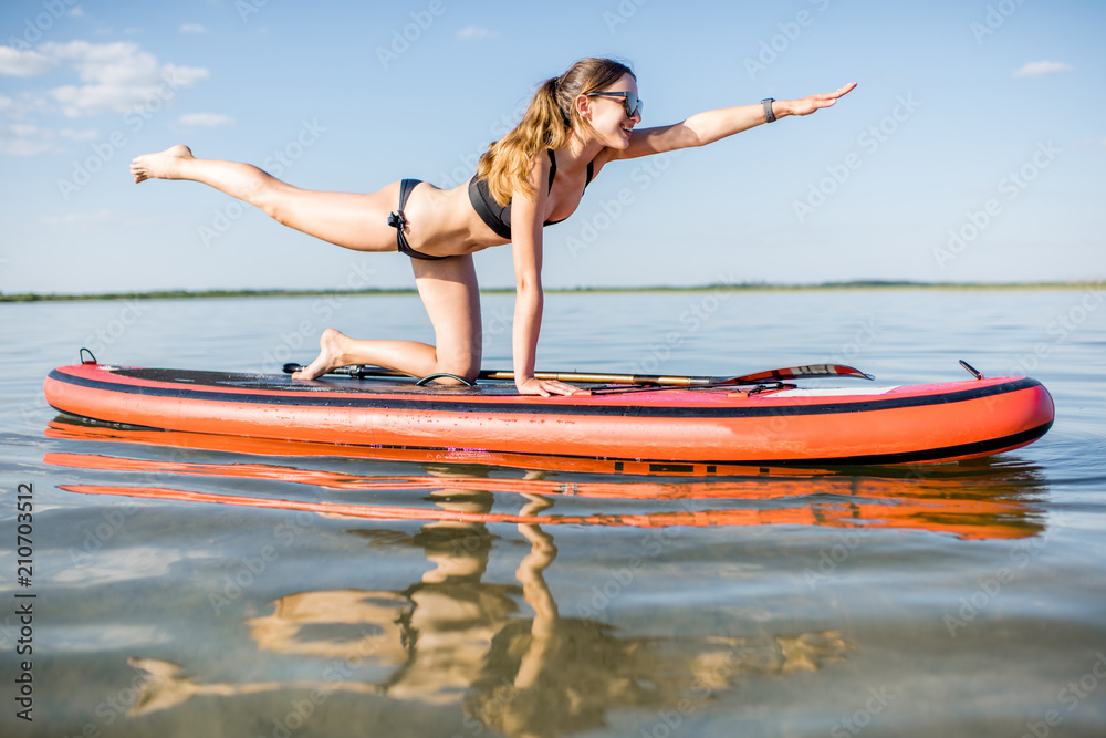 一名年轻女子在湖面上的桨板上做瑜伽，湖面平静，清晨倒影。