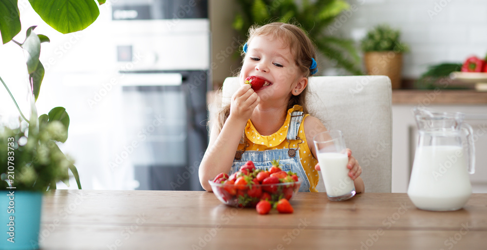 快乐的小女孩吃草莓配牛奶。