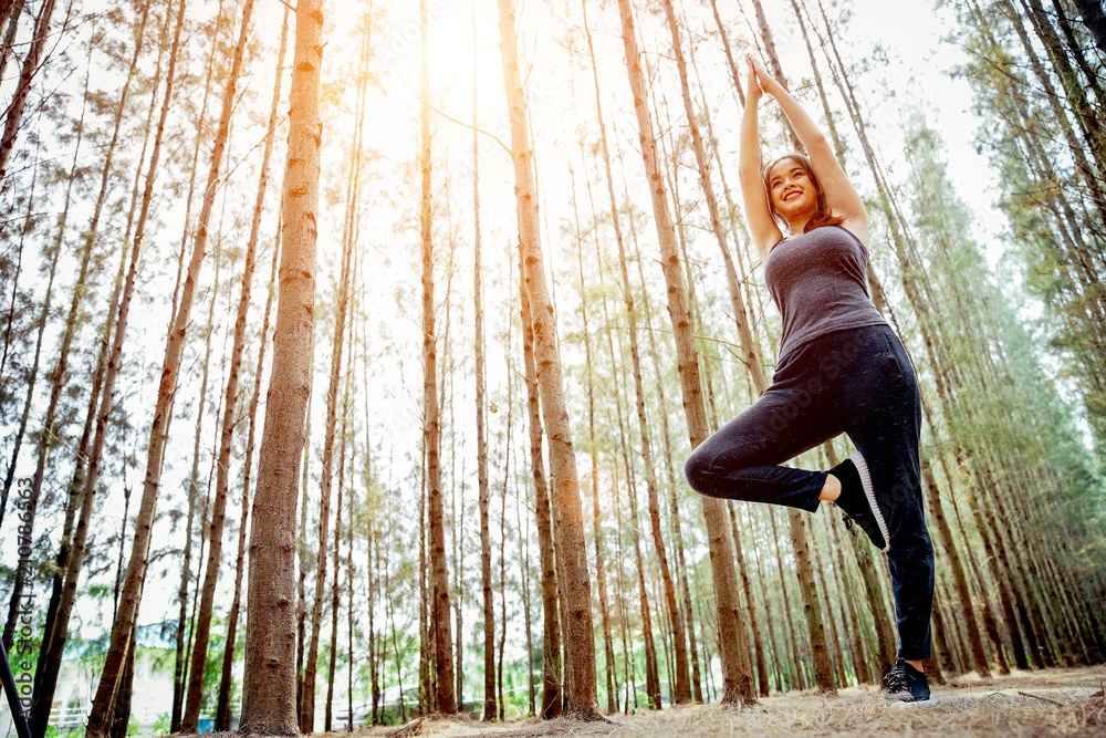 亚洲女孩正在锻炼身体，周末在郁郁葱葱的松林里做瑜伽。