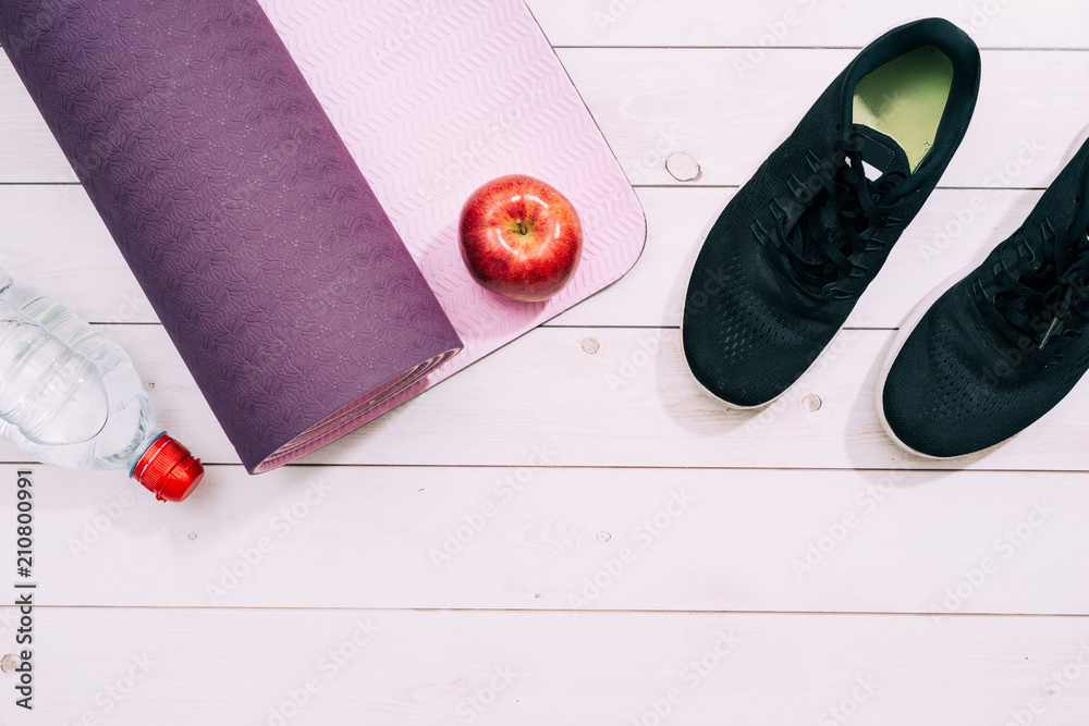女士运动配件，如运动鞋、哑铃、带水和苹果的瑜伽垫。健身，