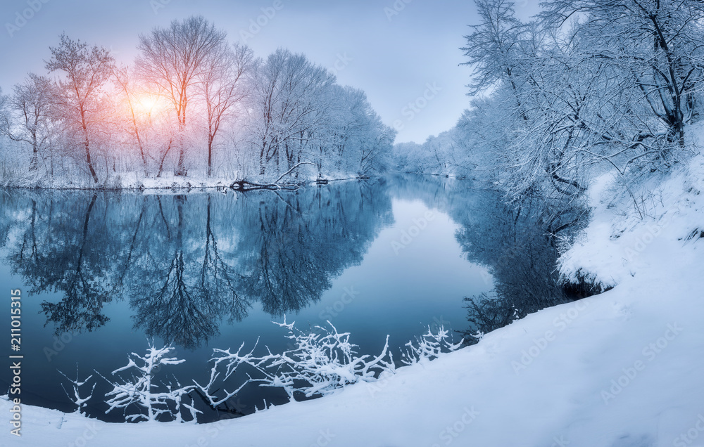 日落时河上的冬日森林。色彩斑斓的风景，白雪皑皑的树木，冰冻的河流，倒影
