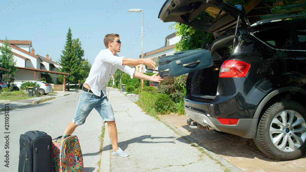 Carefree man throwing travel bags into the back of SUV parked in front of house.