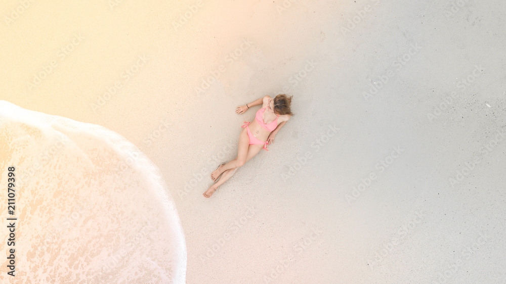 Young asian woman in a bikini lying on the beach  on the white sand near the waves, Aerial top view 
