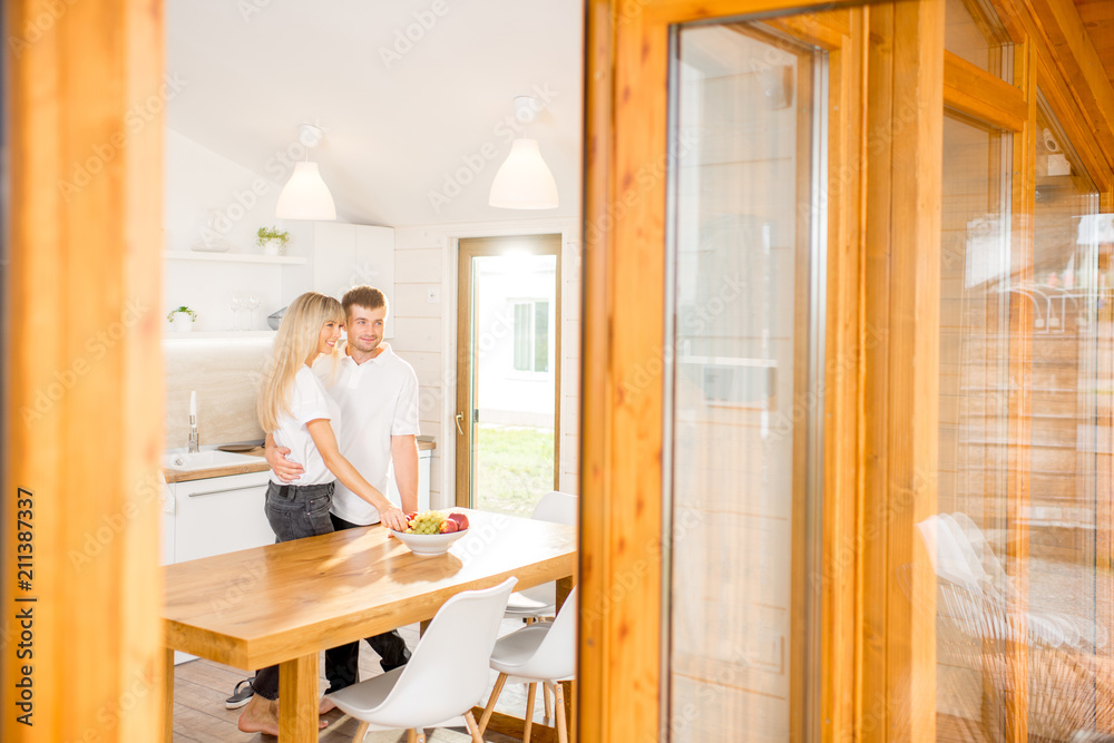 Young couple standing together at the spacious dining room of the modern wooden country house. View 