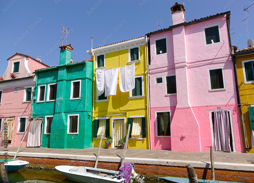 在阳光明媚的威尼斯，一栋五颜六色的房子前，白色的大床单挂在外面晾干。