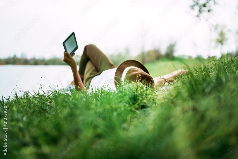 在湖边欣赏电子书。女孩躺在草地上。