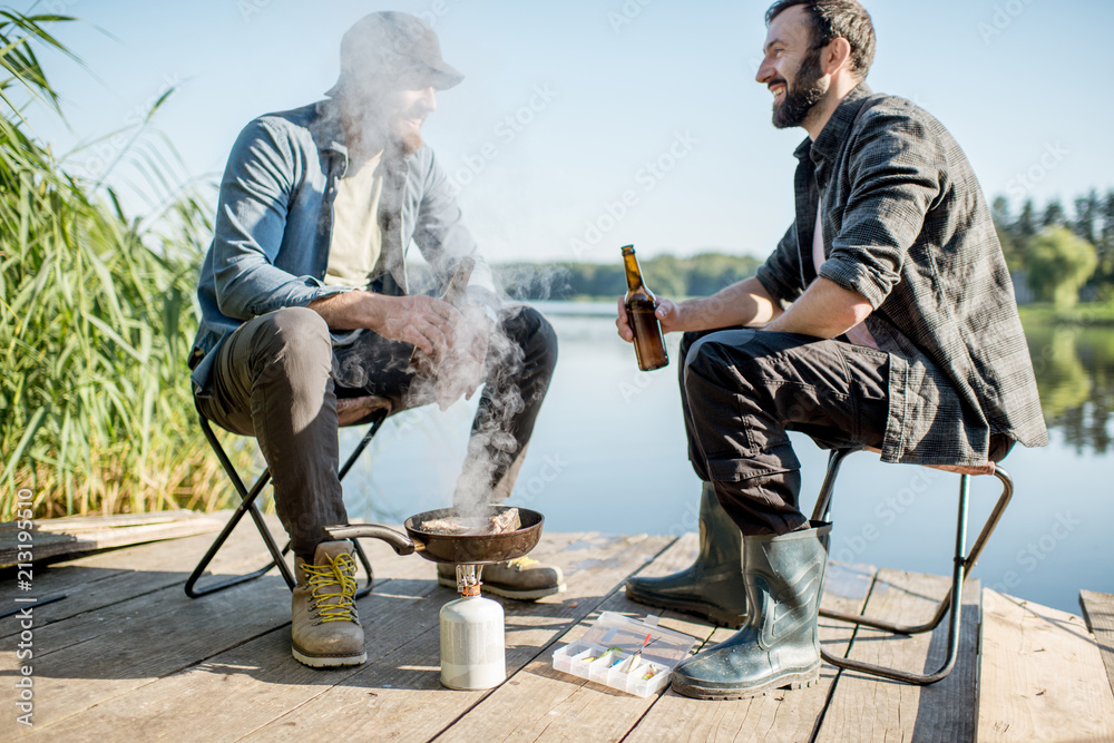 两名渔民在th湖附近的木码头野餐时坐在啤酒里煎鱼