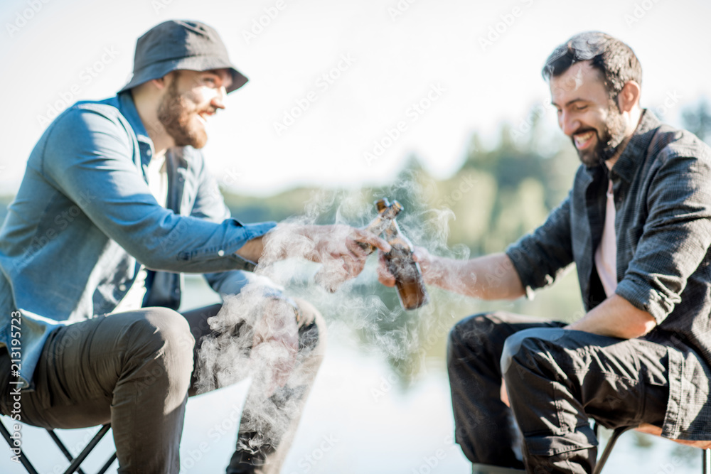 两名渔民在湖边的木码头上野餐时，坐着用啤酒煎鱼