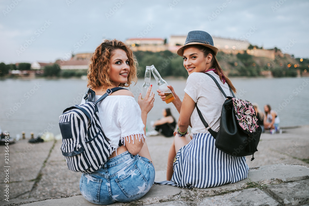 两位时尚的年轻女士坐在河边欢呼。