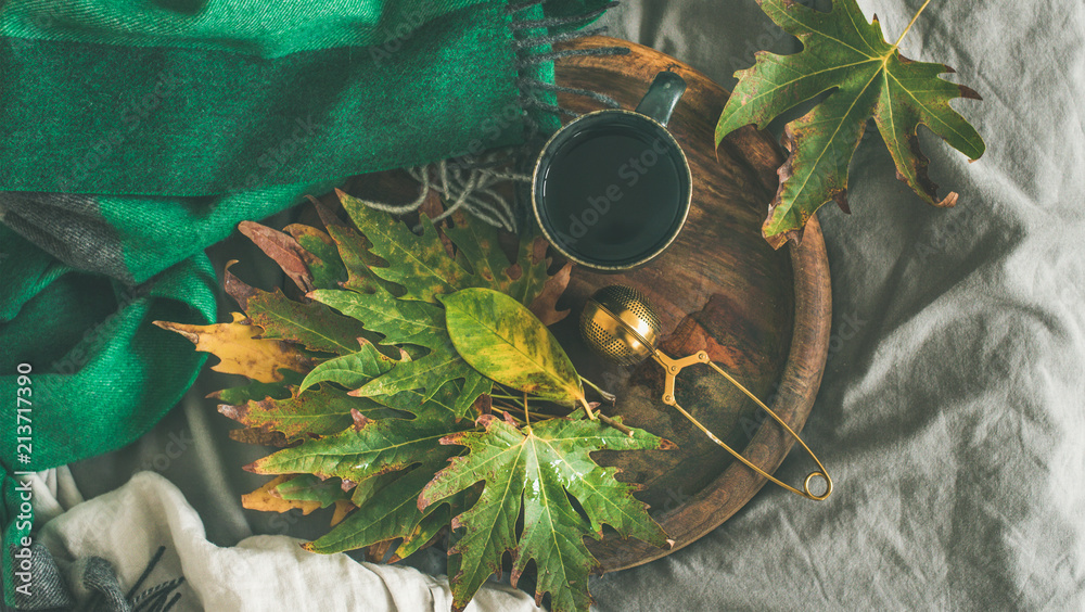 秋天的早茶躺在床上。一杯带筛子的茶平放在乡村的木头上，五颜六色的落叶