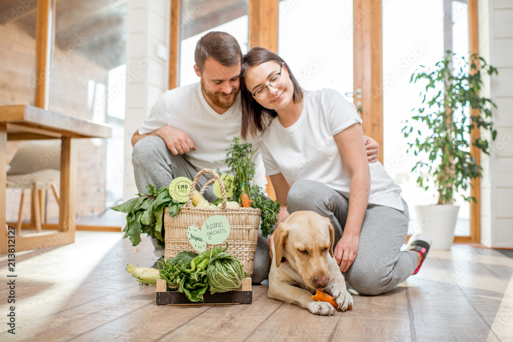年轻可爱的夫妇在家里和他们的狗和新鲜的绿色蔬菜坐在一起