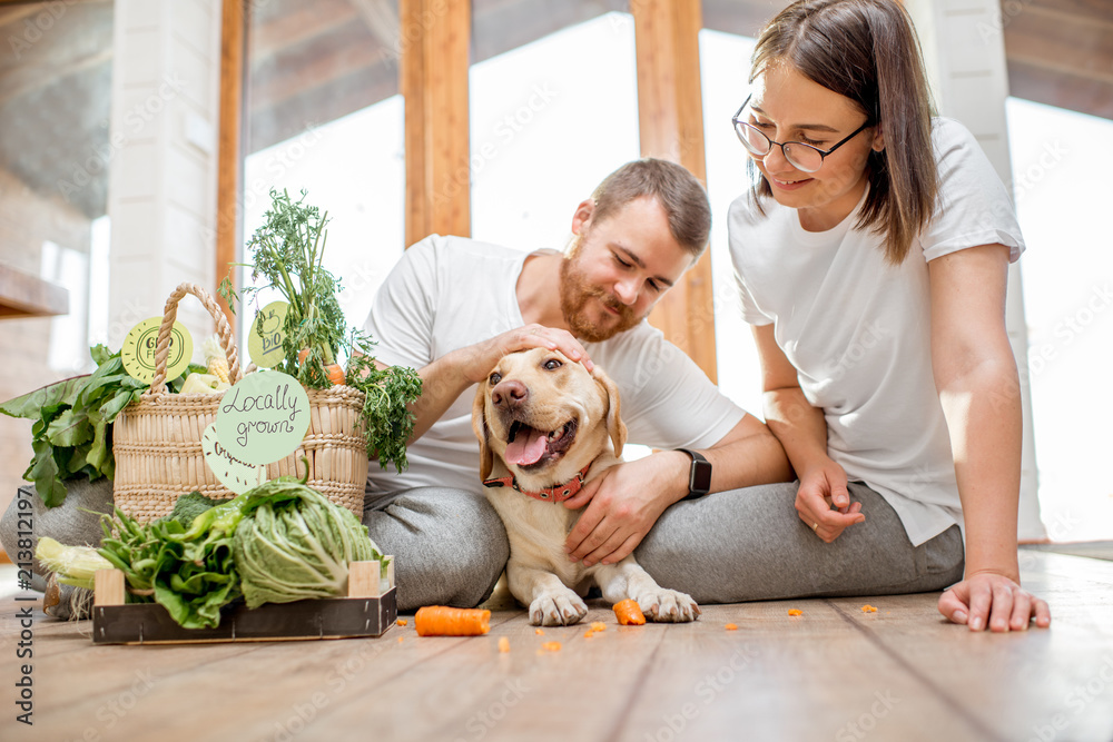 年轻可爱的夫妇在家里和他们的狗和新鲜的绿色蔬菜坐在一起
