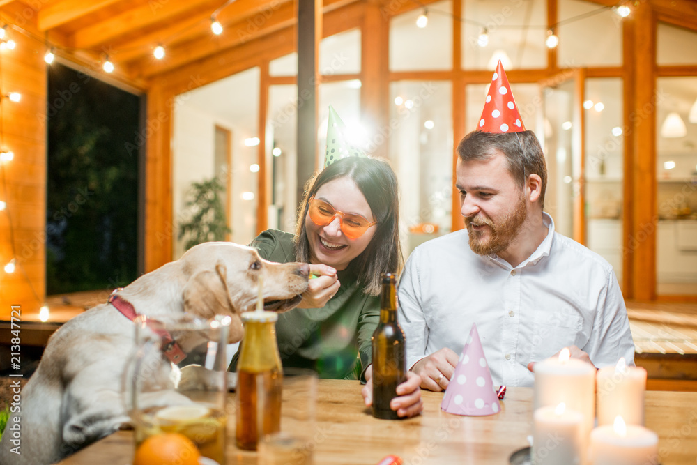 Funny dog with young couple sitting at the table during a celebration on the backyard of the house o