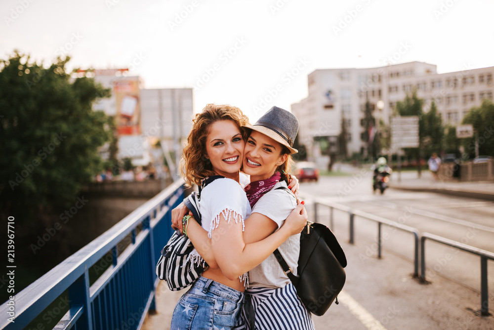 Portrait of a two gorgeous young female friends hugging while standing in the city. Summer music fes