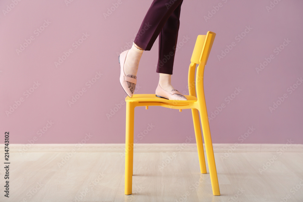 站在靠着彩色墙的椅子上的年轻美女的腿