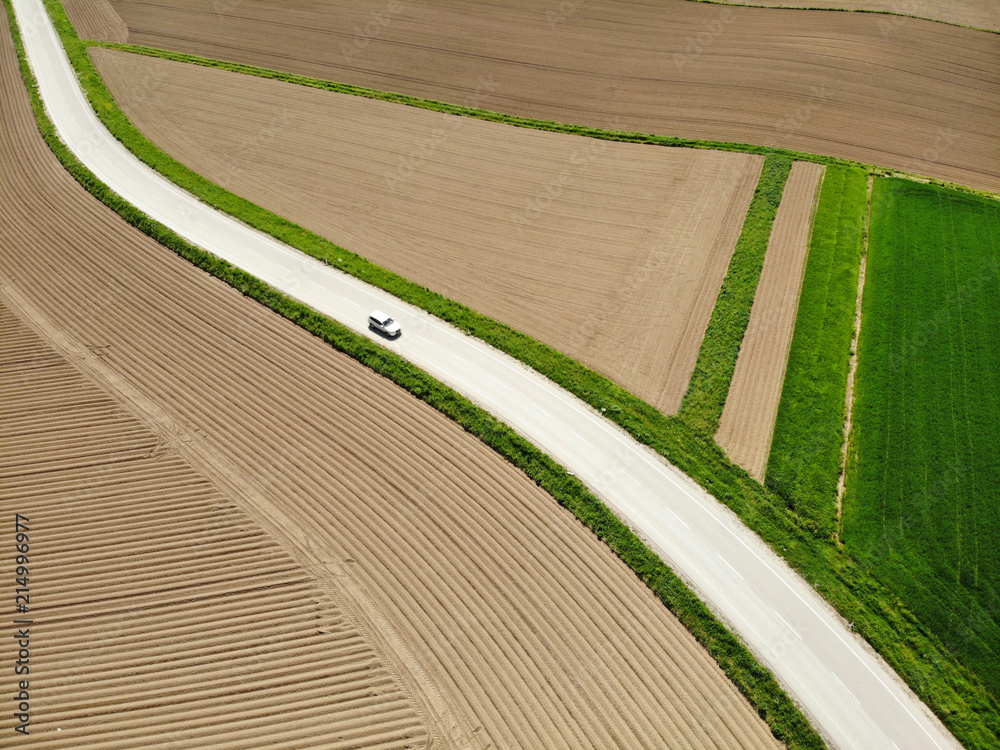 空中交通：一辆白色汽车沿着蜿蜒穿过风景如画的乡村的道路行驶。