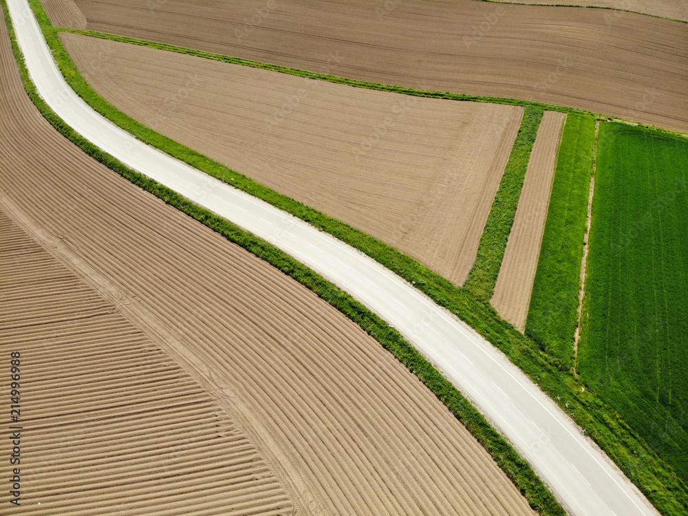 空中：飞过一条经过犁过的田野和草地的柏油路。