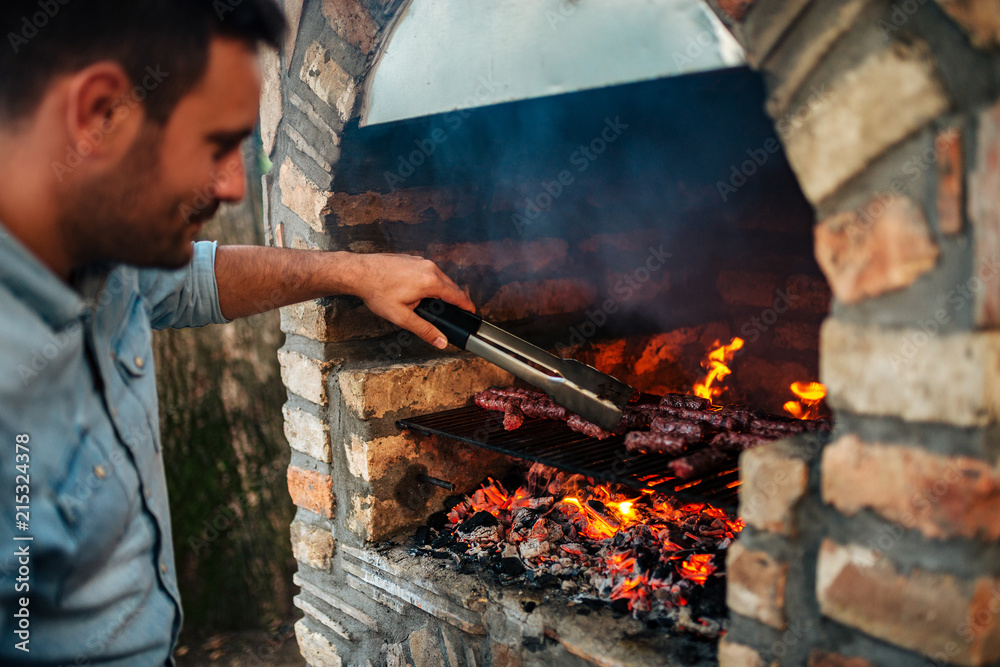 英俊的男人在老式的砖砌烧烤上准备肉。